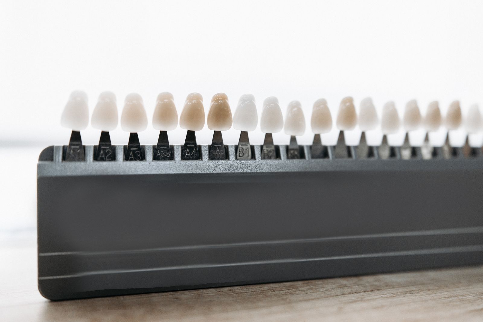 A row of porcelain tooth shade tabs arranged along a tray on a wooden bench.