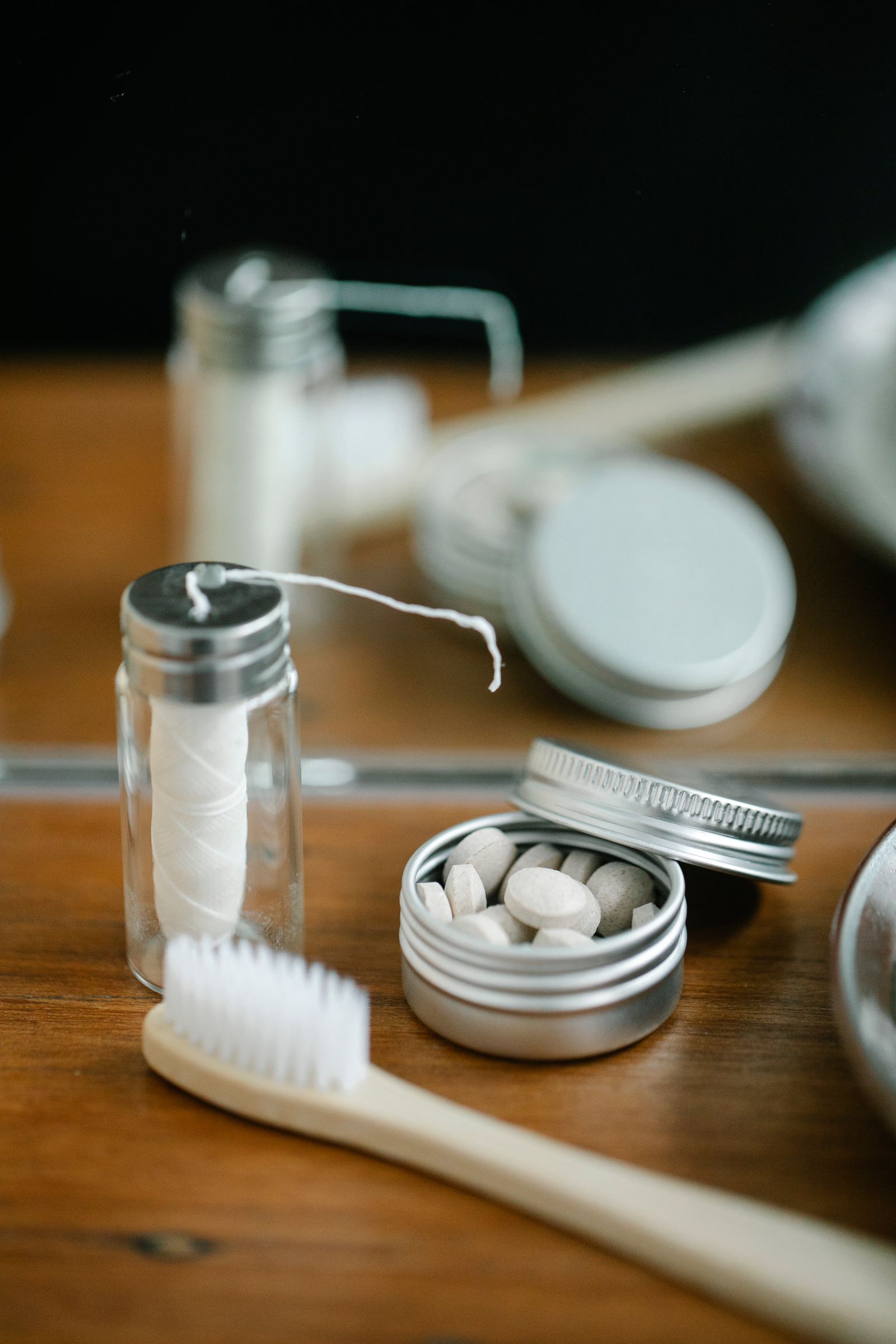 A glass dispenser of dental floss with a strand drawn out, beside lidded jars on a wooden shelf.