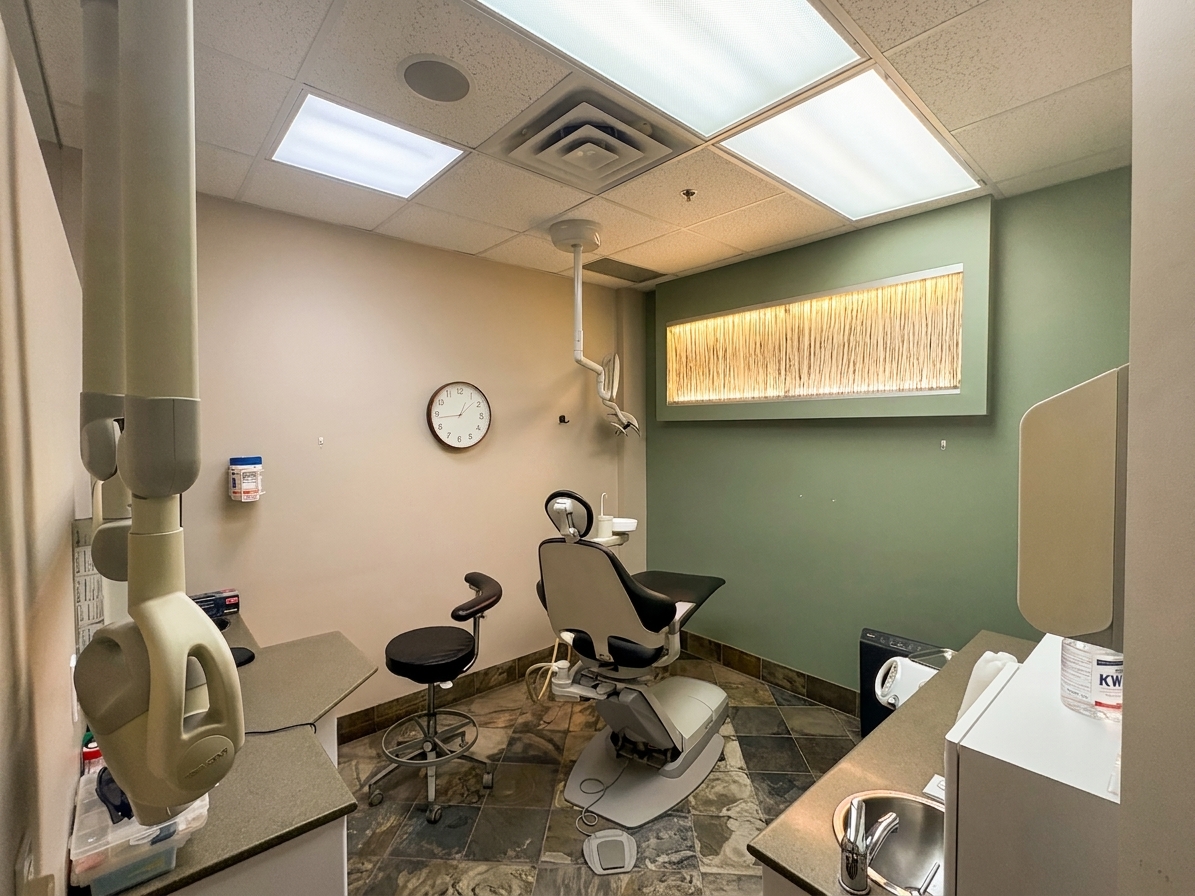 A dental treatment room at Auburn Centre Dental with a patient chair, stool, and a wall clock beside a green accent wall.