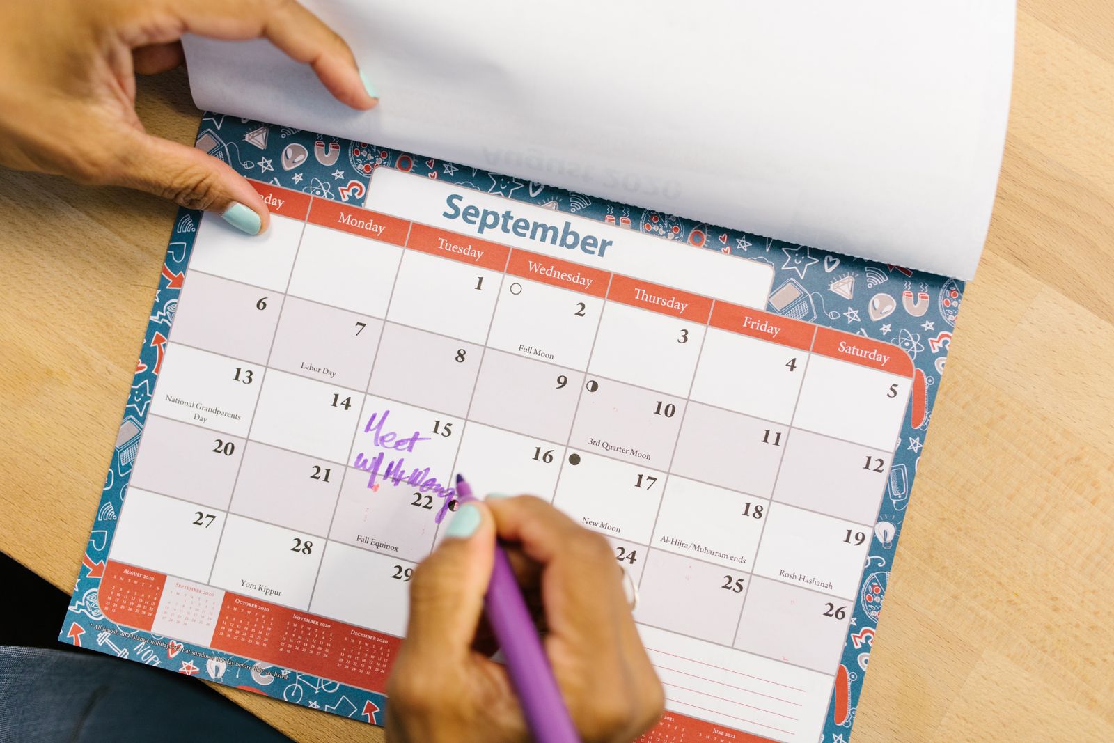 A hand marking a date on a desk calendar with a pen.