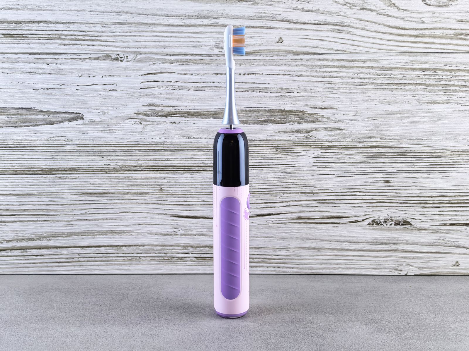An electric toothbrush standing upright against a whitewashed wooden wall.